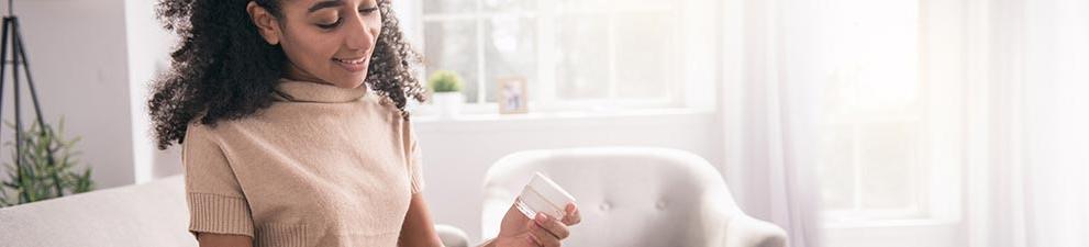 Young woman removes sample jar of cream from a marketing mail parcel.